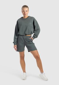 Sudadera recortada de color verde oscuro con dobladillo elástico, combinada con pantalones cortos a juego que tienen una cinturilla elástica. Ambos están hechos de una tela suave.