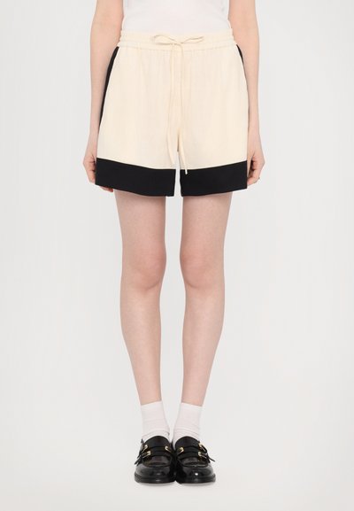 Shorts crème et noir avec une taille élastique et un cordon de serrage. Les shorts présentent un design à blocs de couleur avec une texture lisse.
