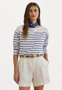 Chemise à rayures à manches longues en crème et bleu, assortie à un short taille haute blanc et une ceinture tissée avec une boucle en métal. Écharpe bleue à fleurs pour l'accent.