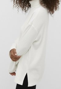 Maglione bianco a collo alto, a costine, con una vestibilità rilassata, caratterizzato da spacchi laterali e maniche lunghe. Realizzato in morbido tessuto a maglia.