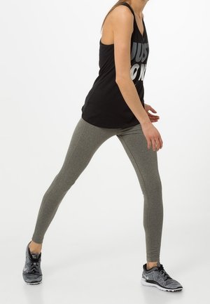 Canotta nera con il bold "JUST DO IT", abbinata a leggings grigi. Una persona in scarpe da ginnastica è in una posa dinamica e attiva.