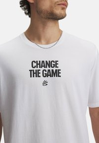 Camiseta de algodón blanca con un atrevido estampado en negro que dice "CAMBIA EL JUEGO". Cuello redondo y mangas cortas. Textura suave.