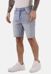 Shorts di denim azzurro chiaro con dettagli strappati, design classico a cinque tasche e passanti per cintura, abbinati a sneakers bianche.