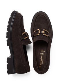 Paire de mocassins en daim marron foncé avec semelles noires épaisses et boucles décoratives en métal bronze, une chaussure vue de dessus, l'autre de côté.