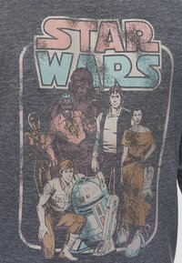 Maglietta grigia con grafica usurata di Star Wars che presenta personaggi iconici. Il design include colori come blu, rosa e dettagli marroni.