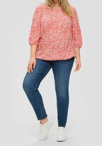 Haut à motifs rouges et blancs avec des manches trois-quarts, associé à un jean skinny bleu foncé et des baskets blanches. Texture lisse, coupe décontractée.