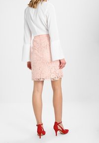 White cropped blouse with pleated sleeves, paired with a pink floral lace skirt and red high-heeled shoes featuring ankle straps.