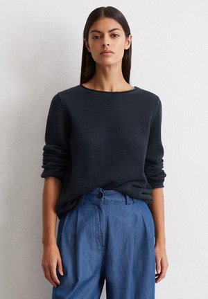 Marineblauwe gebreide trui met een gestructureerd patroon, ronde hals en opgerolde mouwen, gecombineerd met lichtblauwe wijde broek met een knoopdetail.