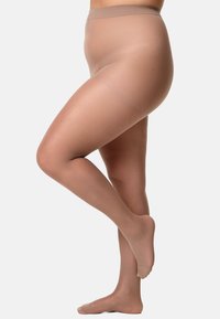 Gambe in collant nudo trasparente, una gamba leggermente piegata con le punte dei piedi rivolte, su uno sfondo chiaro e semplice.