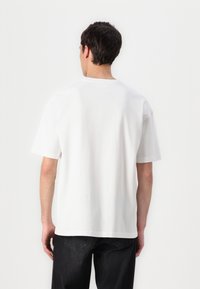 White cotton t-shirt with short sleeves, a crew neckline, and a relaxed fit. Back view shows a smooth texture and minimal design.