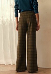 Weite Karottenhosen mit Karo-Muster in gedämpften Grün- und Brauntönen, mit hoher Taille, glattem Stoff und Gesäßtaschen. Darüber ein Pullover in Blaugrün.