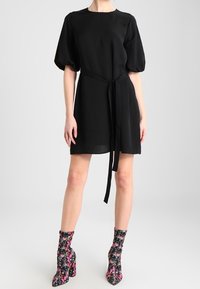 Černé krátké šaty s nabíranými rukávy, páskem v oblasti pasu a hladkou strukturou. V páru s květinovými kotníkovými botami a masivním podpatkem.