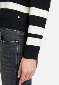 Dunkelblau-weiß gestreifte Pullover mit gerippten Bündchen, aus einem weichen Material gefertigt. Sichtbares goldenes Hardware-Detail an der Saumkante, kombiniert mit dunklen Jeans.