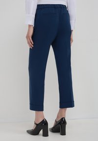 Pantaloni tailored blu navy con una vestibilità rilassata, orli arrotolati, tasche posteriori e vita elastica, abbinati a scarpe nere con tacco.