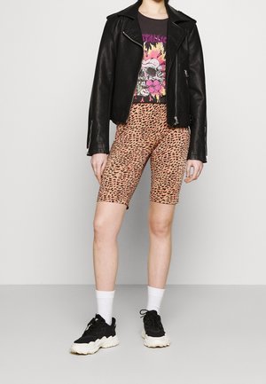 Svart läderbikerjacka, t-shirt med färgglad skalle som motiv och cykelshorts med leopardmönster. Svarta sneakers med vita detaljer.