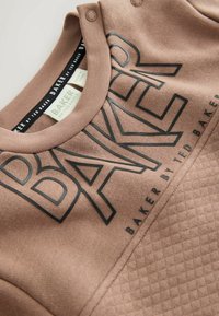 Brązowy sweter z dużym czarnym napisem "BAKER", strukturalną dolną częścią z wzorem diamentowym oraz zatrzaskami przy szyi.