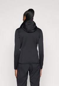 Canguru preto ajustado com uma gola alta e cordão ajustável. Material liso e elástico com costuras planas. Combinado com calças pretas.