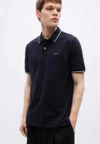 Polo bleu marine avec bordures blanches sur le col et les manches, arborant un petit logo GANT sur la poitrine. Confectionné en tissu texturé.