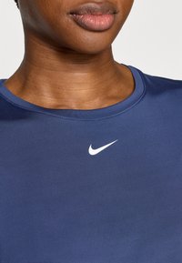 Μπλε ναυτικό αθλητικό πουκάμισο από λείο ύφασμα με στρογγυλή λαιμόκοψη· διαθέτει λευκό λογότυπο Nike στην πάνω αριστερή πλευρά του στήθο υς.