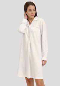 Camisa de noche blanca con lunares rosas, diseño con cuello, mangas largas, bolsillo en el pecho y ribete rosa en contraste a lo largo del cuello y los puños.