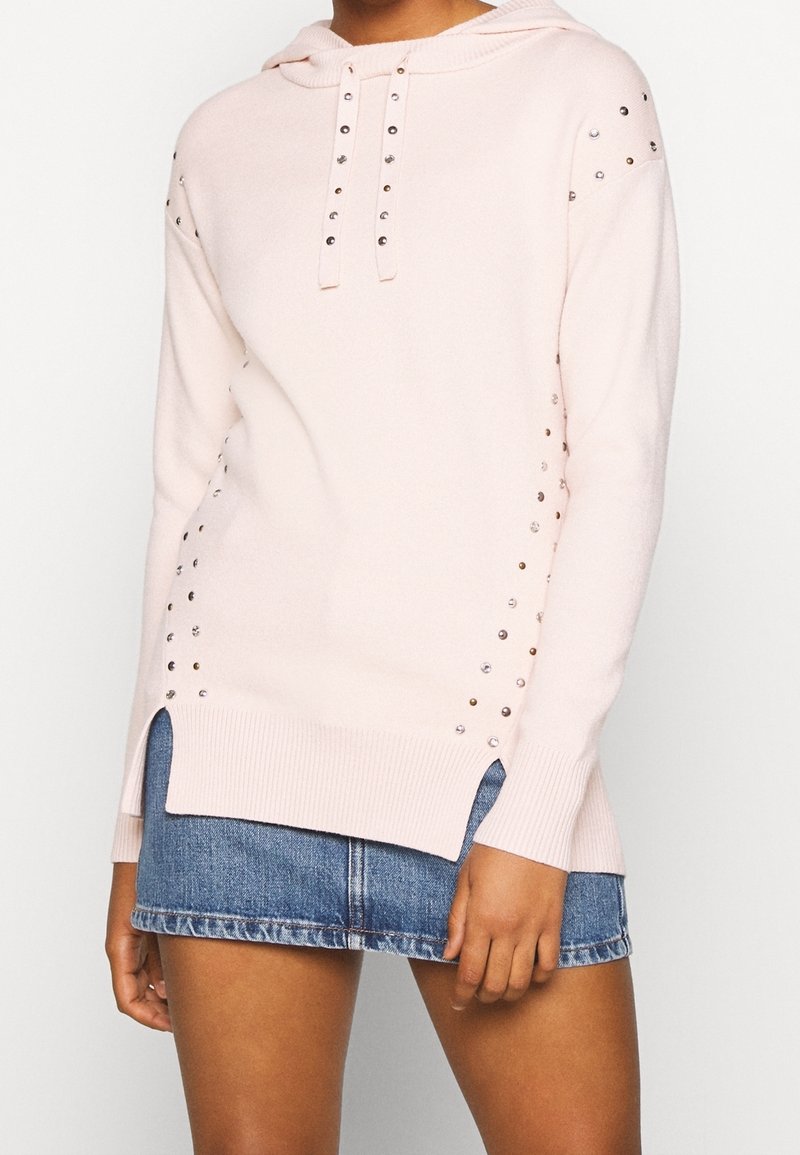 Ljust rosa långärmad tröja med metallspikar längs sidorna och axlarna, tillsammans med en blå denimminikjol.