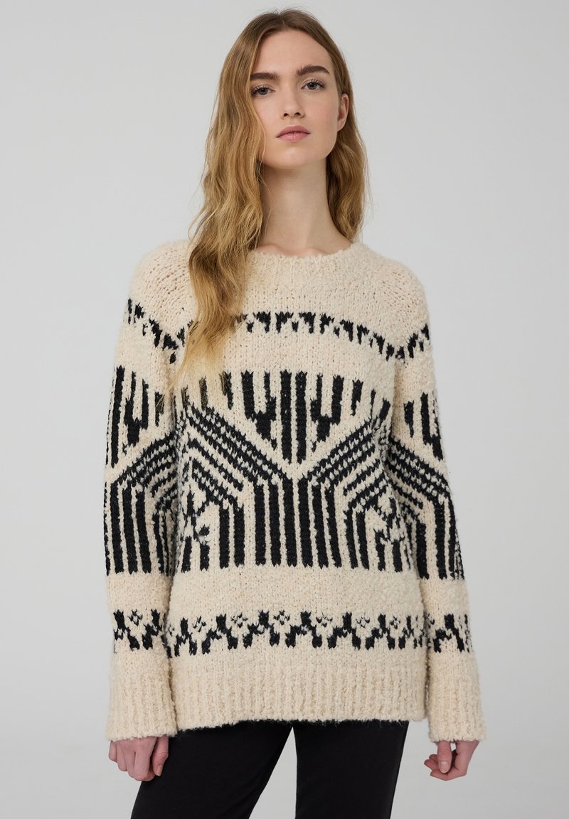 Maglione lavorato a maglia in crema e nero, con motivi geometrici, scollo rotondo e maniche lunghe con polsini a coste. Materiale spesso e testurizzato.