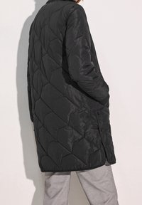 Svart vadderad dunjacka med quiltat diamantmönster, avslappnad passform och långa ärmar. Har en slät yta och knäppning med knappar.