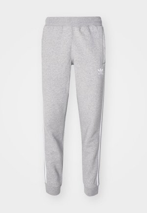 Grå sweatpants lavet af blødt stof, med elastisk talje, sidelommer og hvide striber langs siderne. Adidas-logoet i hvid.