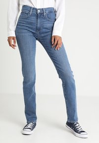 Högmidjade, raka jeans i mellanblå denim med en slät yta. Kombinerade med marinblå canvas-sneakers för kontrast.