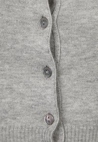 Grå stickad cardigan med fem knappar, ribbat fåll och mjuk textur. Knapparna är runda med subtila designdetaljer.