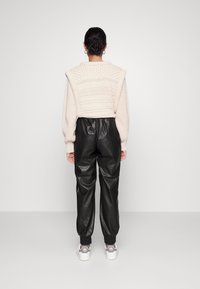 Cream knitted sweater with textured details, paired with black leather joggers and gray sneakers, viewed from the back against a plain background.