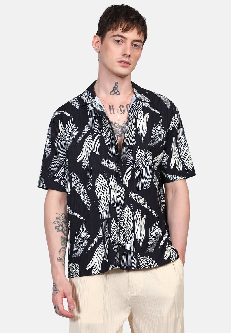 Camicia a maniche corte di colore blu navy con motivi astratti a onde bianche. Presenta un colletto e una vestibilità ampia. Il tessuto sembra leggero e strutturato.