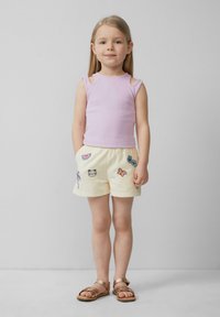 Débardeur côtelé violet clair avec des découpes aux épaules, associé à un short crème orné de motifs brodés colorés. Sandales marron.