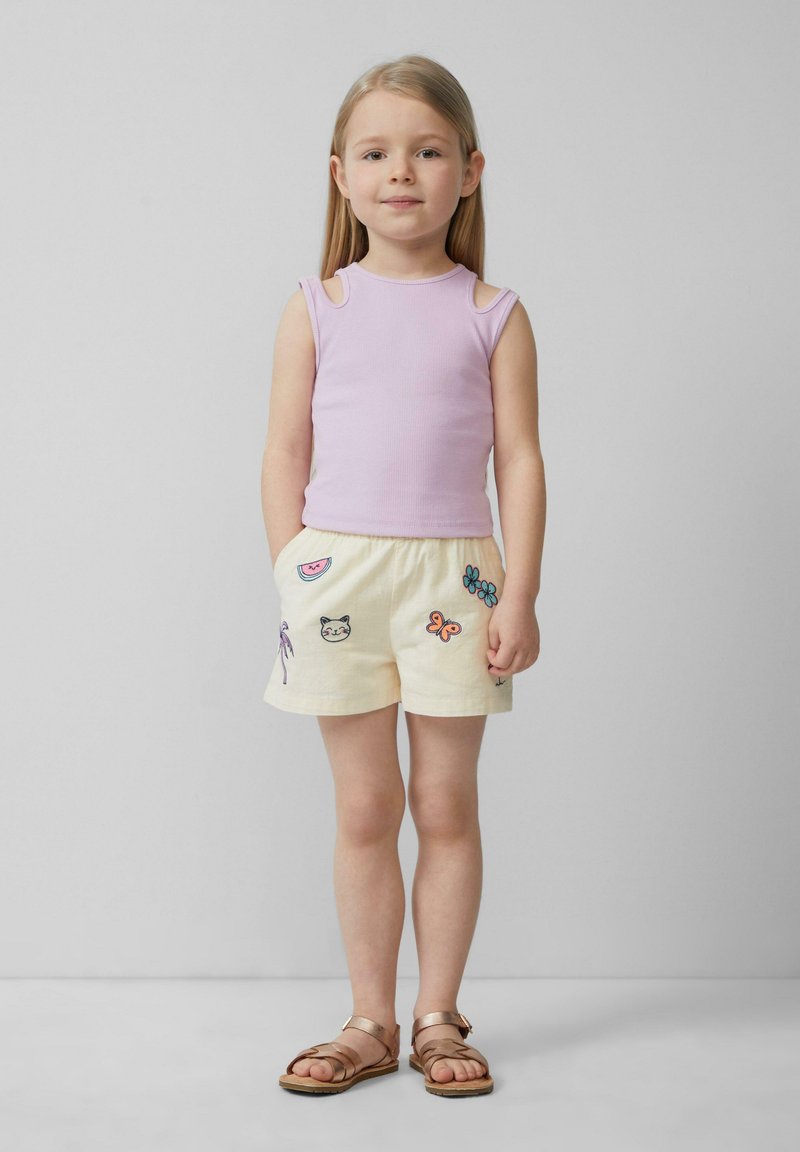 Débardeur côtelé violet clair avec des découpes aux épaules, associé à un short crème orné de motifs brodés colorés. Sandales marron.