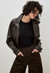 Braune Lederjacke mit einem strukturierten schwarzen Oberteil und braunen Leopardenprint-Hosen. Die Jacke verfügt über einen Kragen und Knopfdetails.