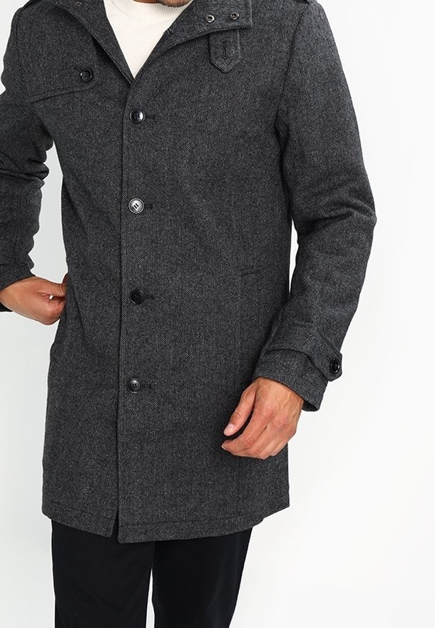 Homme portant un manteau en laine gris foncé boutonné avec une poche poitrine à rabat et des détails de sangles sur le col et les poignets.