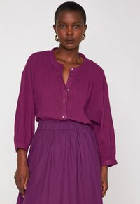 Blusa a maniche lunghe con bottoni e gonna abbinata in un ricco viola con righe sottili. Tessuto morbido, vestibilità comoda e vita elastica sulla gonna.