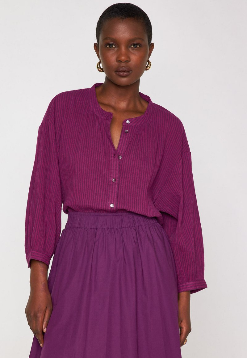 Blusa a maniche lunghe con bottoni e gonna abbinata in un ricco viola con righe sottili. Tessuto morbido, vestibilità comoda e vita elastica sulla gonna.
