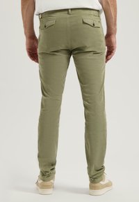 Olívové bavlnené nohavice so slim fit strihom, ktoré majú dve zadné vrecká a zapínanie na gombík, v kombinácii s béžovými teniskami.