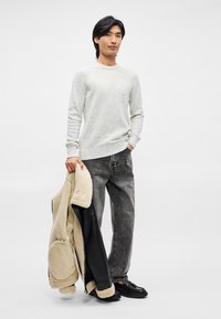 Ανοιχτό γκρι πουλόβερ με κηλίδες, μαύρο δερμάτινο και φλις μπουφάν κρεμασμένο στον ώμο, ξεθωριασμένο γκρι τζιν, μαύρα παπούτσια. Απλή, casual εμφάνιση.