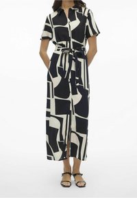 Vestido con estampado en blanco y negro, de mangas cortas, con botonadura frontal, cinturón en la cintura y una abertura. Tela suave con un diseño geométrico.