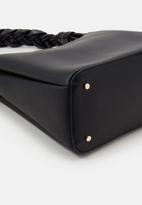 Svart läderhandväska med flätad rem, rektangulär form, texturerad yta och guldfärgade metallfötter i de nedre hörnen.