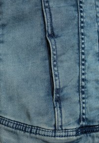 Tessuto di denim blu sbiadito con un dettaglio della tasca e cuciture evidenti, dalla consistenza liscia e leggere variazioni di tonalit�à.