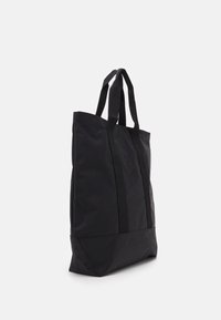 Black tote bag with a simple design, made from durable fabric. Features two long handles and a flat bottom for stability.