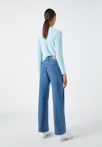 Suéter azul claro, esponjoso, de manga larga, combinado con unos pantalones vaqueros de tiro alto y pierna ancha de mezclilla azul. Unas deportivas blancas con plataforma completan el conjunto.