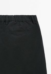 Zwarte katoenen shorts met een elastische tailleband, voorzien van een platte achterzak en een gladde textuur. Eenvoudig ontwerp zonder extra patronen.