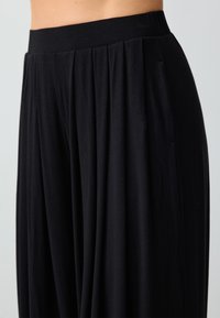 Pantalons larges noirs en tissu doux, dotés d'une taille haute élastique et d'un devant plissé pour un ajustement décontracté et une silhouette drapée.