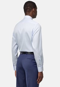 Camisa de vestir a rayas azul claro con mangas largas y puños abotonados. Combinada con pantalones oscuros, que cuentan con dos bolsillos traseros y un cinturón negro.