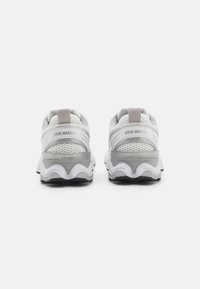 Scarpe da ginnastica grigie e bianche con parte superiore in rete testurizzata, suola curva distintiva e morbido tab di supporto sul tallone; marchio visibile sul retro.