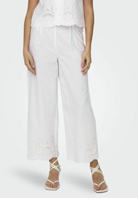 Witte, wijde broeken met geborduurde eyelet-details aan de zoom, gecombineerd met witte strap sandalen. Zachte stof en een relaxte pasvorm.